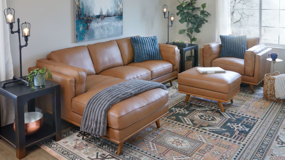 Camel colored brown leather sectional accompanied by matching chair and ottoman in blue and brown toned living room window scene