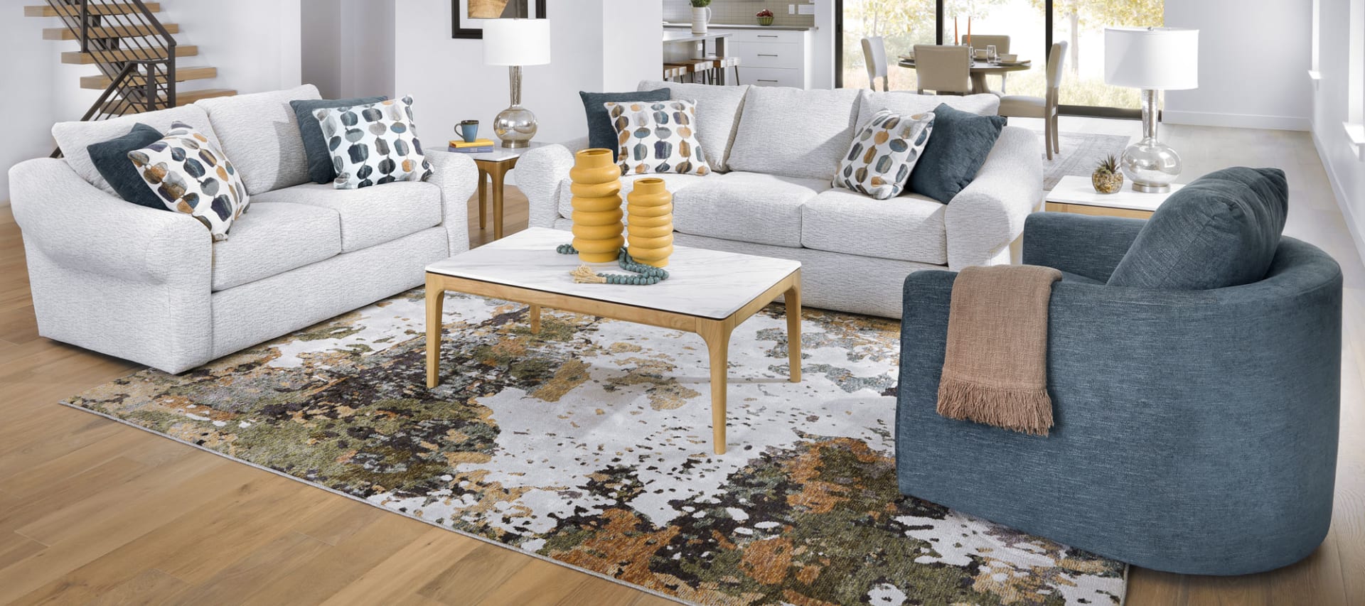 A contemporary sitting group featuring light-colored sofas, a dark blue accent chair, and a white coffee table. The sofas have large curved arms and the chair has a round back.